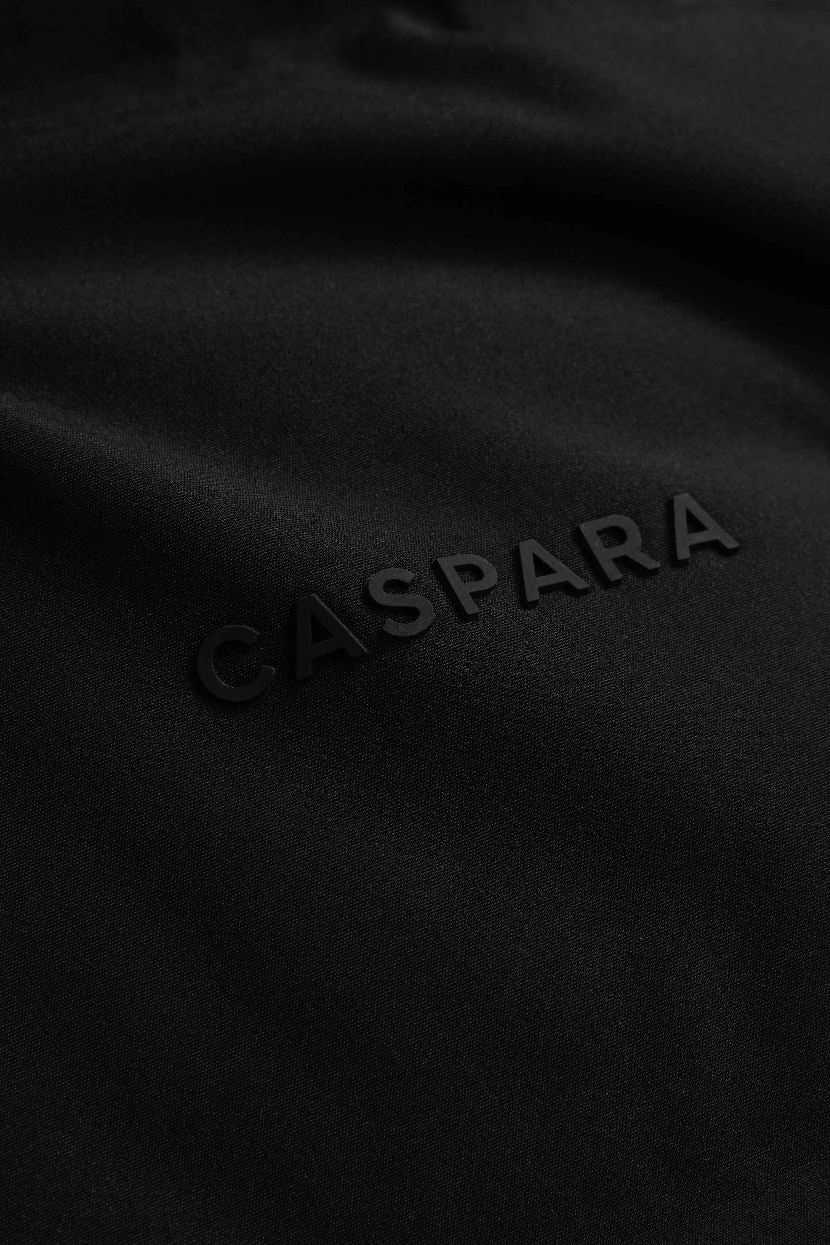 Close-up of the raised CASPARA logo on the black Boreal Puffer Jacket.
